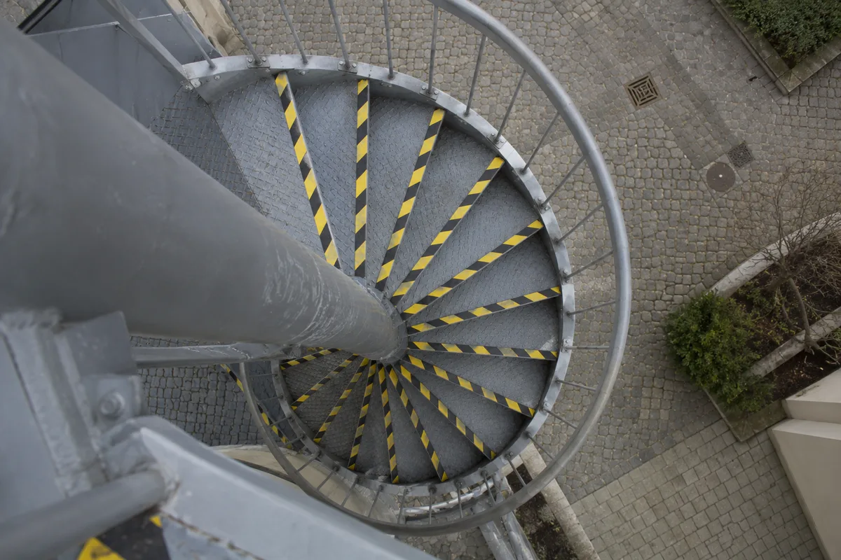 Escalier hélicoïdal extérieur en acier peint gris vu de dessus, bandes jaunes et noires au bord de chaque marche